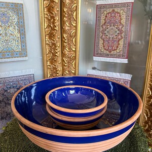 Może przedstawiać: Zestaw trzech niebieskich ceramicznych misek umieszczonych w większej misce z beżową krawędzią. Miski ułożone są na zielonej, koralikowej powierzchni, z dekoracyjnymi, oprawionymi miniaturowymi dywanami w tle.