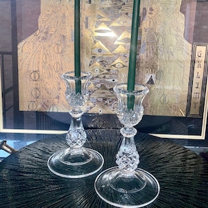 Op de afbeelding: Twee heldere glazen kaarsenstandaards met een diamantpatroon op een zwart oppervlak. Elke standaard heeft een groene kaars erin.