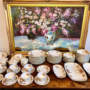 Könnte beinhalten: Ein Vintage-Porzellan-Tee-Set mit floralen Mustern in Blau-, Orange- und Grüntönen. Das Set beinhaltet eine Teekanne, eine Milchkännchen, eine Zuckerdose, Tassen, Untertassen und Teller. Das Set wird auf einem Holztisch mit einem Blumenbild im Hintergrund präsentiert.