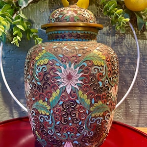 May include: A cloisonné vase with a lid, featuring a floral design in shades of blue, green, red, and white on a brown background.