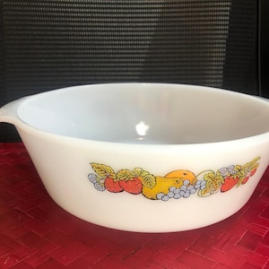 Puede incluir: Cuenco mezclador Pyrex blanco con un diseño de frutas colorido. El cuenco presenta un borde de fresas, uvas y otras frutas. El cuenco tiene un asa a cada lado.