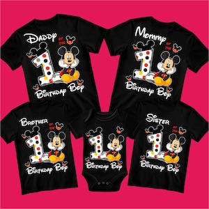 May include: Black family birthday shirts and a onesie featuring Mickey Mouse. Each shirt has a large number 1 with polka dots, Mickey Mouse, and the words "Daddy", "Mommy", "Brother", and "Sister". The onesie says "Birthday Boy".