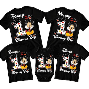 May include: Black family birthday shirts and a onesie featuring Mickey Mouse. Each shirt has a large number 1 with polka dots, Mickey Mouse, and the words "Daddy", "Mommy", "Brother", and "Sister". The onesie says "Birthday Boy".