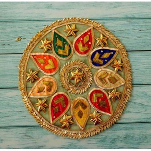 Pode incluir: Uma peça decorativa circular com uma borda dourada e um design de formas de lágrima em várias cores, incluindo vermelho, laranja, amarelo, verde, azul e rosa. As formas de lágrima são decoradas com bordados dourados e lantejoulas.