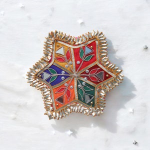 May include: A colorful star-shaped decorative object with a silver border. The star is made of fabric and has a geometric pattern with mirrors and beads.