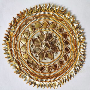 May include: A circular gold and silver decorative embellishment with a floral design. The embellishment has a layered pattern with a central flower surrounded by concentric circles of smaller flowers and beads.