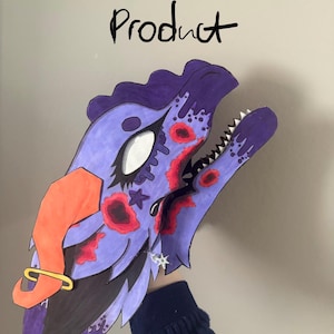 May include: A purple paper dragon mask featuring red circular patterns, a large white eye, a jagged mouth with white teeth, an orange horn, and a gold hoop earring. The text "Not the Product" is written in black ink above the mask.