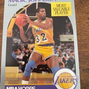 Puede incluir: Una tarjeta de baloncesto con Magic Johnson con el uniforme de Los Angeles Lakers. La tarjeta tiene el texto "MOST VALUABLE PLAYER" y "NBA HOOPS". Johnson lleva una camiseta amarilla y morada con el número 32.