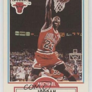 Puede incluir: Una tarjeta de colección vintage con Michael Jordan, un jugador de baloncesto de los Chicago Bulls. La tarjeta es roja, blanca y azul con una foto de Jordan en el aire, haciendo un mate. La tarjeta tiene el texto "Chicago Bulls" y "Michael Jordan" en ella.