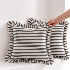 May include: Two square throw pillows featuring a black and off-white horizontal striped pattern. Each pillow is finished with a gathered fabric ruffle trim along all four edges, creating a textured border around the striped center panel.