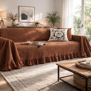 May include: A brown sofa with a ruffled cover and a decorative pillow featuring a black and white floral design. The sofa is in a well-lit living room with plants and a wooden coffee table.