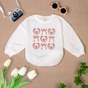 May include: White long-sleeved sweatshirt with a crew neck and a repeating pattern of pink bows with lace trim.