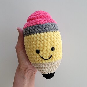 May include: A crocheted pencil plush toy with a pink eraser, yellow body, and a smiling face.