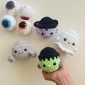 Op de afbeelding: Een verzameling handgemaakte Halloween-speeltjes van gehaakt garen. De speeltjes omvatten oogballen, een vampier, een spook, een Frankenstein-monster en een grijze alien. De speeltjes zijn gemaakt van zacht garen in diverse kleuren.