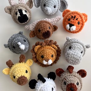 Pode incluir: Uma coleção de dez cabeças de animais feitas de crochê com fio de pelúcia macio. O conjunto inclui uma cabra, elefante, tigre, vaca highland, rinoceronte, leão, hipopótamo, girafa, zebra e urso, cada um com pequenos olhos de plástico preto.
