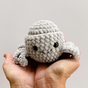 May include: A handmade, gray crocheted octopus plush toy with black button eyes and a smiling mouth. The octopus has a textured, soft appearance and is held in open hands. This adorable toy is perfect for children.