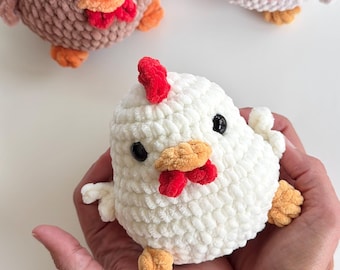 May include: Three round, plush, crocheted chicken toys made from soft, textured yarn. Each chicken features a white, light brown, or dark brown body, a bright red comb, a small orange beak, red wattles, and black plastic bead eyes.