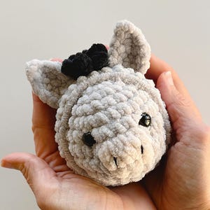 May include: A gray crocheted stuffed animal with black eyes and a black bow on its head. The animal has a small, crocheted snout.