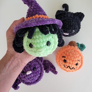 May include: Four crocheted Halloween decorations: a witch with a purple hat and green face, a black cat, a purple bat, and an orange pumpkin.