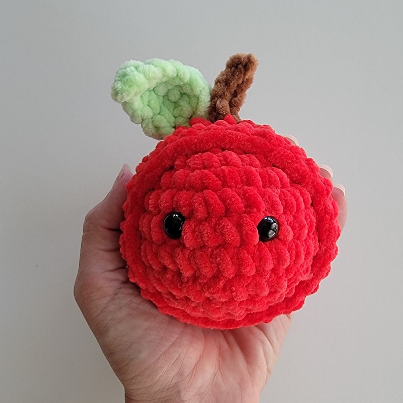 May include: A red crocheted apple with a green crocheted leaf and black eyes.