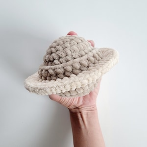 May include: A crocheted hat in the shape of a planet, with a light brown top and a cream-colored bottom.