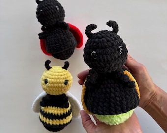 May include: Three crocheted plush toys shaped like insects. One is a black ladybird with red wings, one is a yellow and black striped bee with white wings, and one is a black bug with yellow-orange wings and a light green bottom section.