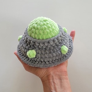 May include: A gray crocheted UFO with a green crocheted dome and green crocheted details.