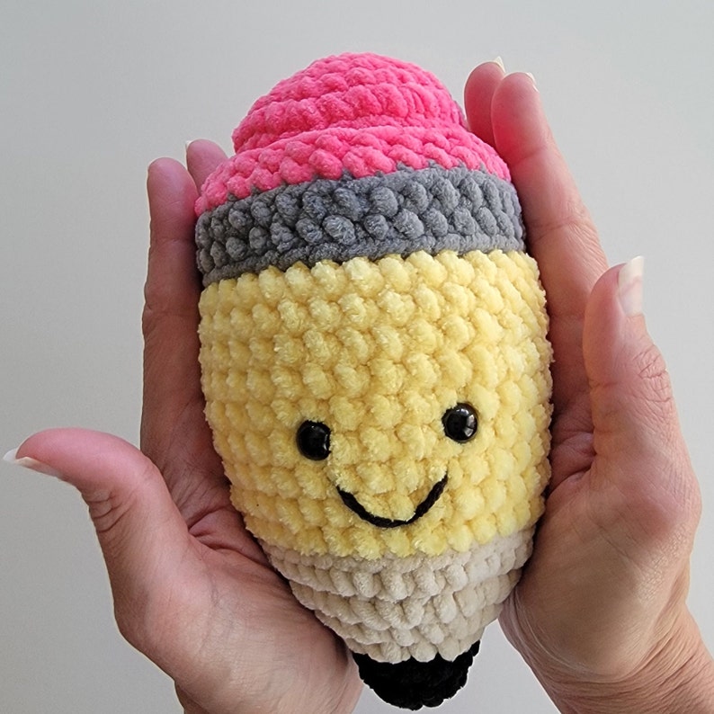 May include: A crocheted pencil plush toy with a pink eraser, yellow body, and a smiling face.