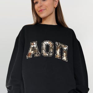 May include: Black sweatshirt with a large, gold and brown camouflage print of the letters "AOP" on the front.
