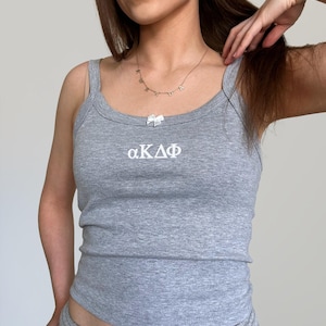 May include: A gray tank top with a white bow and the letters "αΚΔΦ" embroidered on the front.