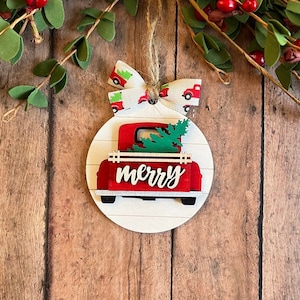 May include: Red wooden Christmas ornament shaped like a pickup truck carrying a small green Christmas tree. The truck has the word "merry" written on the back.