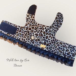 May include: Leopard print dog harness with black ruffle trim and a gold metal D-ring. The harness has a black velcro strap and a label that reads "With love by Evie Beavie".
