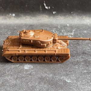 Könnte beinhalten: Ein kleiner, einfarbig brauner Spielzeugpanzer aus Kunststoff mit einem detaillierten Turm, einem langen hervorstehenden Geschützrohr und einer Reihe von Rädern entlang der Kettenlaufwerke. Das Miniaturfahrzeug zeigt sichtbare Luken und Deckdetails.