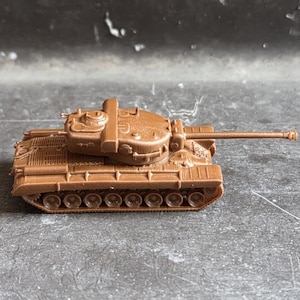 Könnte beinhalten: Ein kleines, einfarbig braunes Kunststoffmodell eines Panzers mit drehbarem Turm, einem langen Hauptgeschützrohr und detaillierten Ketten mit mehreren Laufrollen an der Seite. Das militärische Miniaturfahrzeug ist in einer einzigen Farbe gegossen.