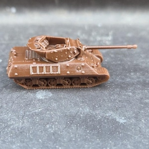 May include: A small brown tank model with a long barrel and detailed tracks. The toy tank has a turret and rectangular openings on the side. The model is a toy or collectible item.