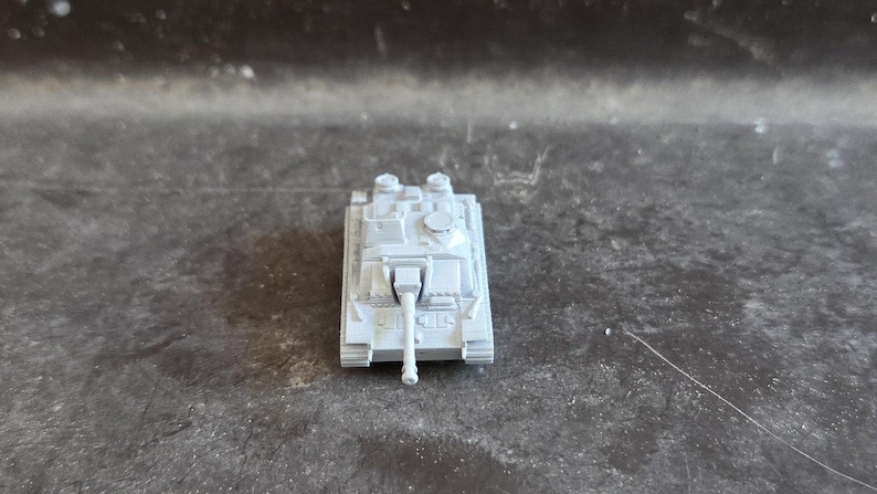 Puede incluir: Un peque&ntilde;o tanque de juguete gris claro con un ca&ntilde;&oacute;n largo y detalles. El modelo en miniatura tiene un cuerpo rectangular, dos torretas y orugas. El tanque est&aacute; sobre un fondo oscuro y texturizado.