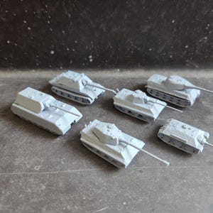 Può includere: Sei piccoli carri armati giocattolo grigio chiaro sono disposti su una superficie scura. Ogni carro armato ha un design distinto, tra cui torrette e canne di fucile. I carri armati sono repliche in miniatura, probabilmente per giocare o esporre.