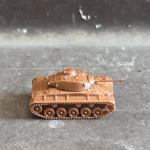 Peut inclure: Un petit modèle réduit de char en plastique marron non peint, doté d'une tourelle centrale, d'un canon court orienté vers l'avant et de chenilles latérales détaillées avec plusieurs roues. Ce véhicule militaire miniature est moulé en une seule couleur.