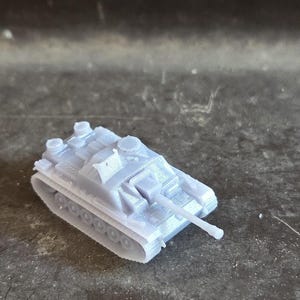 Puede incluir: Un peque&ntilde;o tanque de juguete gris claro con un ca&ntilde;&oacute;n largo y un dise&ntilde;o de oruga detallado. El veh&iacute;culo militar en miniatura est&aacute; hecho de pl&aacute;stico y se encuentra sobre una superficie texturizada. El tanque es un modelo o art&iacute;culo de colecci&oacute;n.