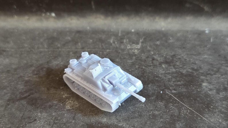 Puede incluir: Un peque&ntilde;o tanque de juguete gris claro con un ca&ntilde;&oacute;n largo y un dise&ntilde;o de oruga detallado. El veh&iacute;culo militar en miniatura est&aacute; hecho de pl&aacute;stico y se encuentra sobre una superficie texturizada. El tanque es un modelo o art&iacute;culo de colecci&oacute;n.