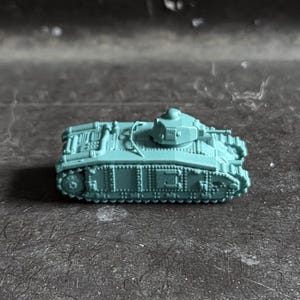 May include: A small, light blue-green scale model tank featuring detailed tracks, a central turret, and a riveted hull design. The miniature military vehicle is cast in a solid, matte-finish material, showcasing intricate mechanical components.