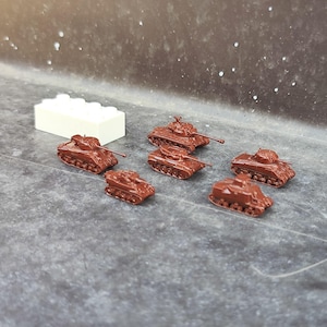 以下が含まれることがあります： 灰色の表面に、大砲が付いた茶色のミニチュア戦車が7台並んでいます。背景には白いレゴブロックがあります。