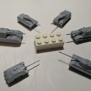 Puede incluir: Seis tanques de juguete grises dispuestos en círculo alrededor de un bloque de Lego blanco. Los tanques tienen diferentes diseños y todos miran hacia adentro.