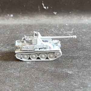 Könnte beinhalten: Ein kleines, unlackiertes hellgraues Modell eines selbstfahrenden Artilleriefahrzeugs. Der Miniaturpanzer verfügt über ein langes, nach vorne gerichtetes Kanonenrohr, einen detaillierten offenen Mannschaftsraum und ein Kettenfahrwerk.