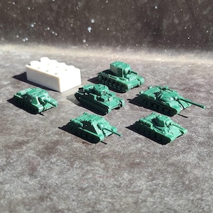 May include: A collection of seven miniature green toy tanks. The tanks are made of plastic and have different designs.