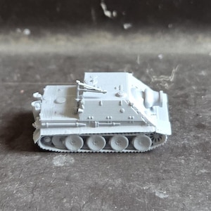 Könnte beinhalten: Ein kleines, unlackiertes hellgraues Kunststoffmodell eines Jagdpanzers mit einer geneigten Frontpanzerplatte, einem kurzen Geschützrohr und einem detaillierten Kettensystem mit mehreren sichtbaren Laufrollen an der Seite des Fahrzeugchassis.