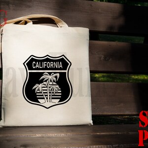 May include: A white tote bag with a black and white graphic of a California road sign with palm trees and the text "CALIFORNIA".