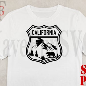 May include: A white t-shirt with a black and white graphic of a California state park emblem. The emblem features a mountain range, a bear, and the text "CALIFORNIA".