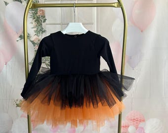 May include: A black and orange tulle dress with long sleeves. The dress has a black bodice and a tulle skirt that is layered with black and orange tulle.