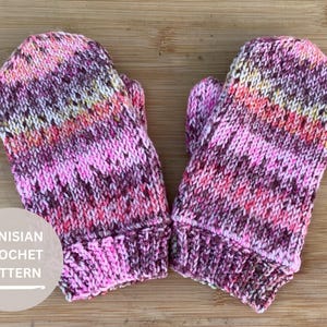 Puede incluir: Un par de manoplas tejidas a mano con un patrón de hilo jaspeado en tonos rosa, morado, naranja y blanco. Las manoplas tienen un puño acanalado y una parte superior redondeada. Un círculo a la izquierda muestra el texto TUNISIAN CROCHET PATTERN.